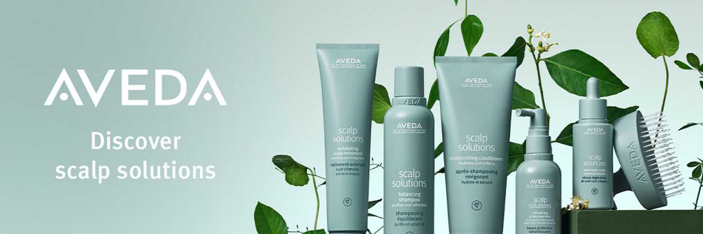 Aveda hair care products arranged with green leaves on a pastel background.