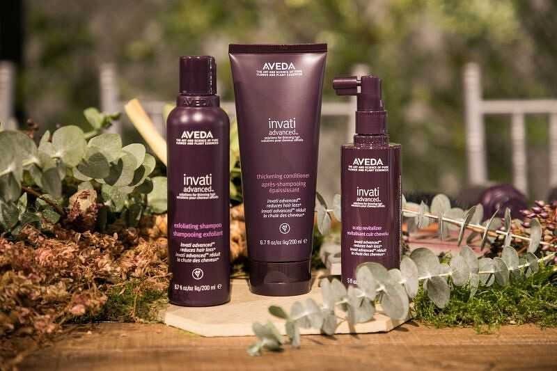 Aveda hair care products displayed among greenery on a wooden surface.