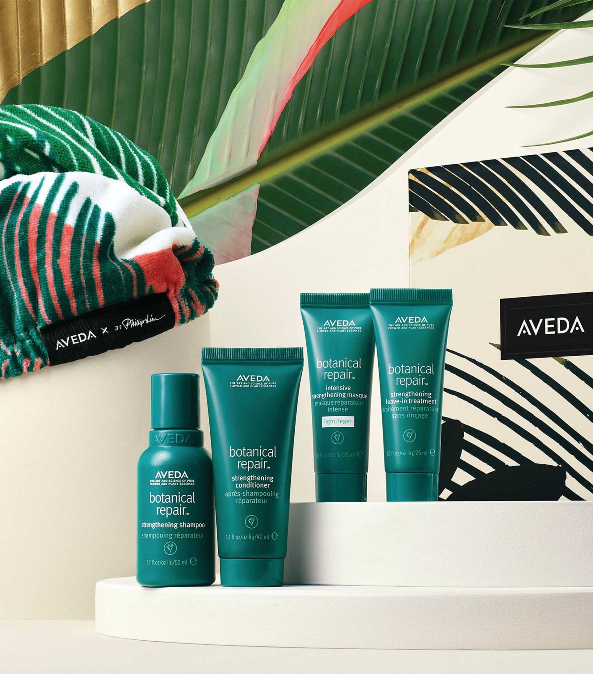 Aveda hair care products arranged artistically with tropical foliage.